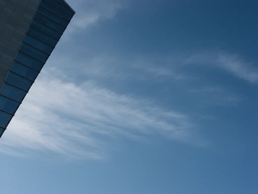 Deep blue sky with soft cirrus clouds framed by the edge of a modernist tower